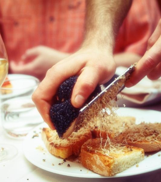 Affettare tartufo nero su crostini, accompagnato da bicchiere di vino bianco.